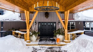 A wooden covered entrance with a black door, snow-covered ground, and potted plants on either side. - Whitestone Ranch | Luxury Lakefront Estate Near Muskoka (Sleeps 24) (Dunchurch)