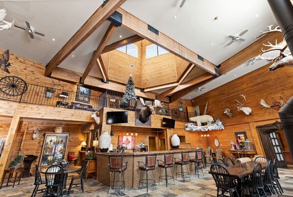 A spacious interior with high ceilings, wooden beams, a central bar area, and various mounted animal heads.