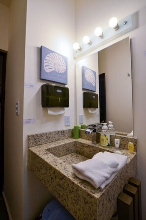 Une salle de bain avec un lavabo en granit, une serviette, un miroir avec éclairage intégré et un distributeur de savon fixé au mur.