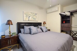 Une chambre à coucher comprenant un lit, deux tables de chevet, une commode, un climatiseur fixé au mur et une étagère avec divers objets.