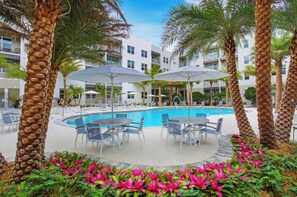 A pool area with lounge chairs and umbrellas, surrounded by palm trees and a building with balconies. - Luxury 2-Bedroom Downtown Sarasota Residence with Resort-Style Amenities (Sarasota)