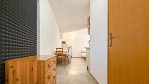 A narrow hallway with a wooden dresser, a chair, a bed, and a desk with a computer. - Americana Karlobag Apartments (Karlobag)