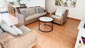 Ein Wohnzimmer mit Rattanmöbeln, einem runden Couchtisch und einem Essbereich mit Stühlen und einem Tisch.