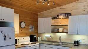 A kitchen with wooden ceiling, white cabinets, a stove, a sink, and a clock.
