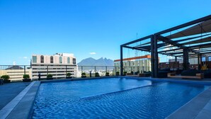 Una piscina en la azotea con vistas despejadas a montañas y edificios al fondo.