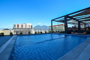 Ein Pool auf dem Dach mit freiem Blick auf Berge und Gebäude im Hintergrund.