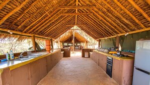 An open-plan kitchen with a thatched roof, stone flooring, and basic amenities. - Private Bush Camp With Pool Cottages Tents - 2332 (Bisil)