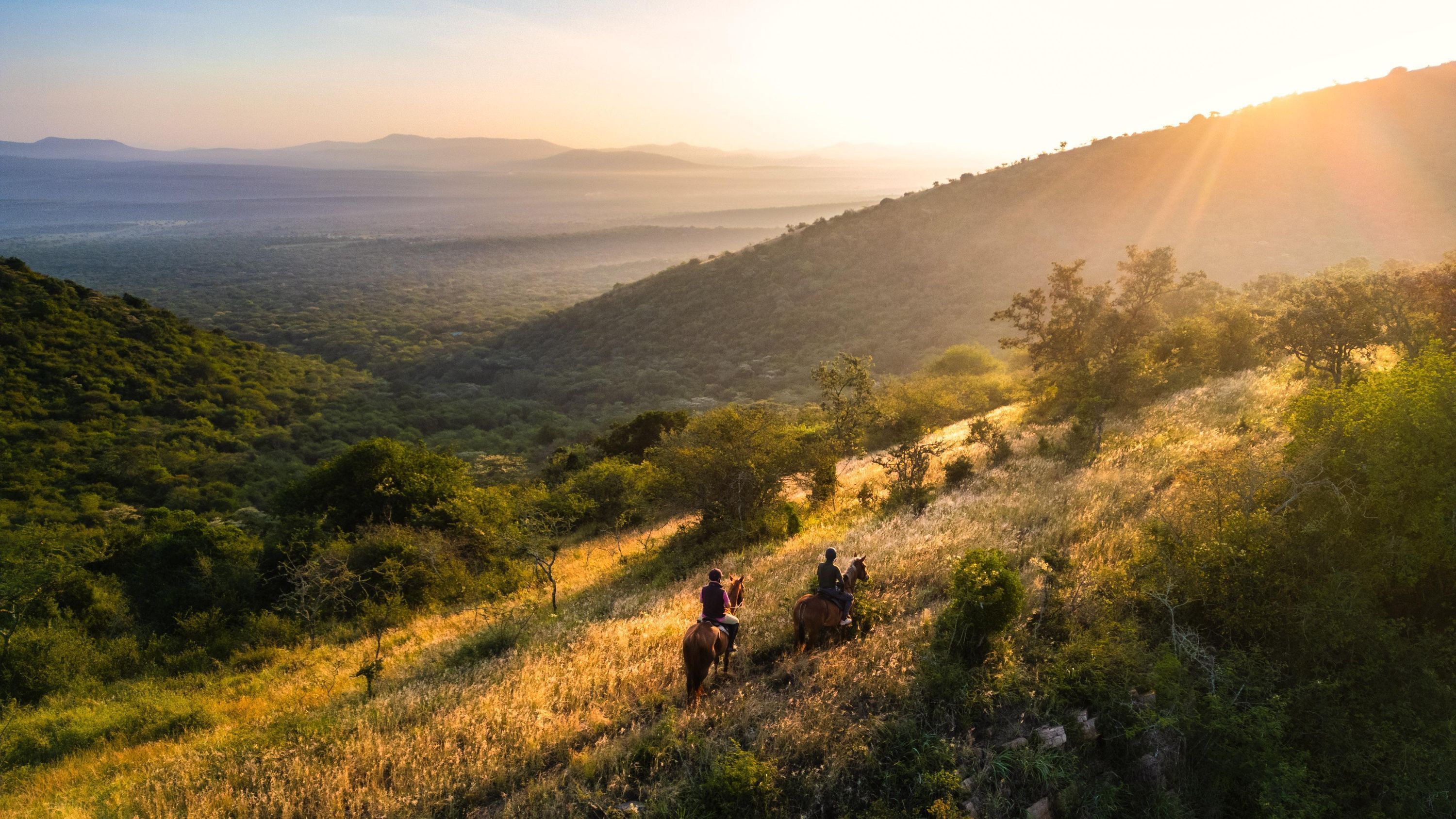 A mountainous landscape with two people riding horses.