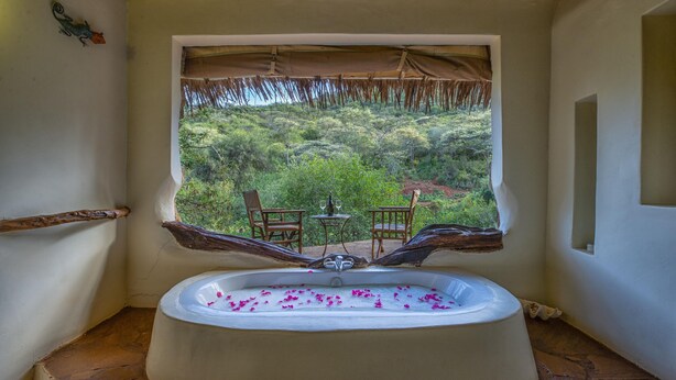 A bathroom with a bathtub, a window with a view of greenery, and two chairs outside. - Private Bush Camp With Pool Cottages Tents - 2332 (Bisil)