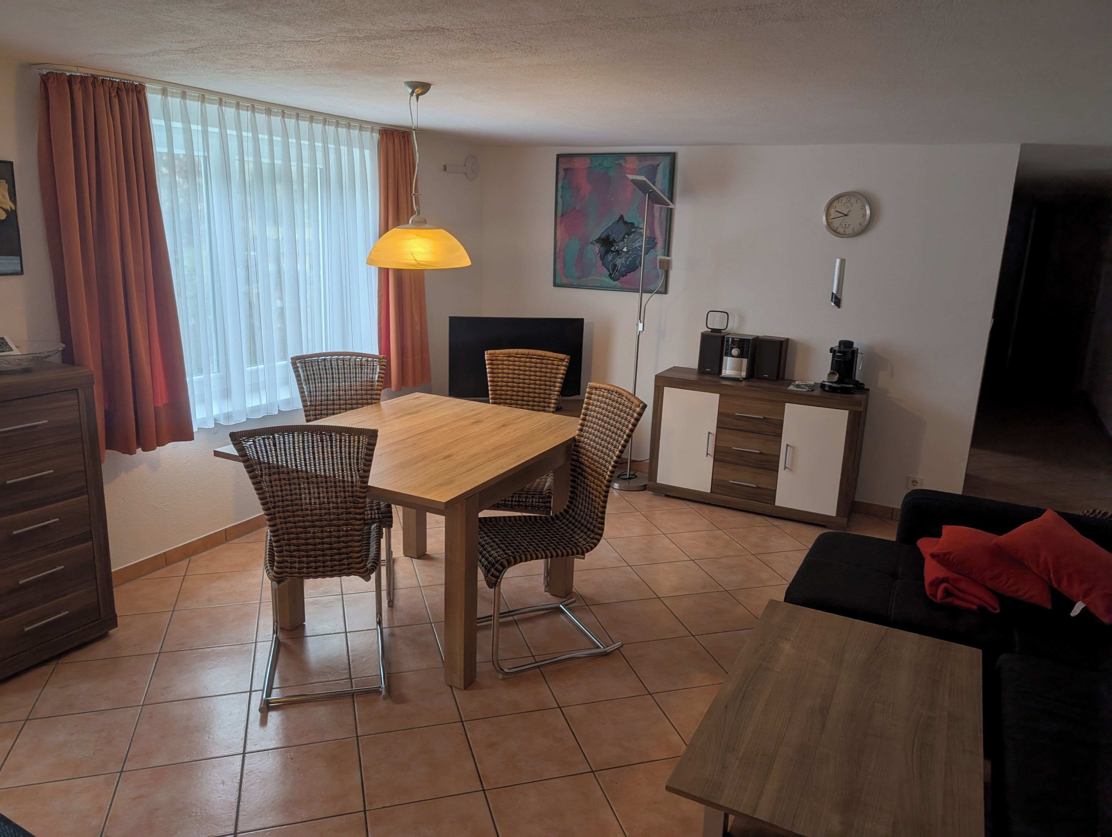 Un coin repas avec une table en bois et des chaises en osier, un meuble contenant une machine à café et un tableau accroché au mur.