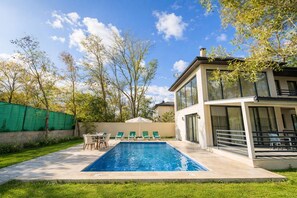 A modern house with a swimming pool, a patio with chairs, and a green fence. - Villa Ana With 3 Bedrooms and 3 Bathrooms (Ortaca)