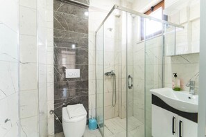 Une salle de bain moderne avec une douche à parois de verre, des toilettes blanches et un lavabo avec un miroir.