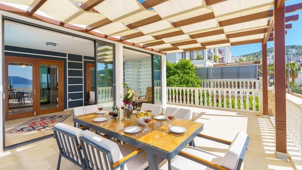 An outdoor dining area with a table set for four, a pergola overhead, and a view of the sea. - Villa Kuluhana With 3 Bedrooms and 3 Bathrooms (Kaş)