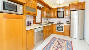 A kitchen with wooden cabinets, stainless steel appliances, a dishwasher, and a patterned rug. - Villa Kuluhana With 3 Bedrooms and 3 Bathrooms (Kaş)