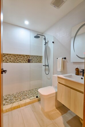 A modern bathroom with a glass-enclosed shower, a toilet, a sink with a mirror, and a wooden cabinet. - Tulum Experience Penthouse Downtown Pool View (Santo Domingo)