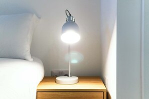 A bedside table with a lamp, a bed, and a wall socket. - Stunning 2 BED Manchester Apartment w City Views (Manchester)
