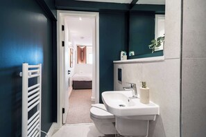 A narrow bathroom with a white sink, toilet, and towel rack. A mirror reflects part of the room, and a door leads to another area. - Stunning 2 BED Manchester Apartment w City Views (Manchester)