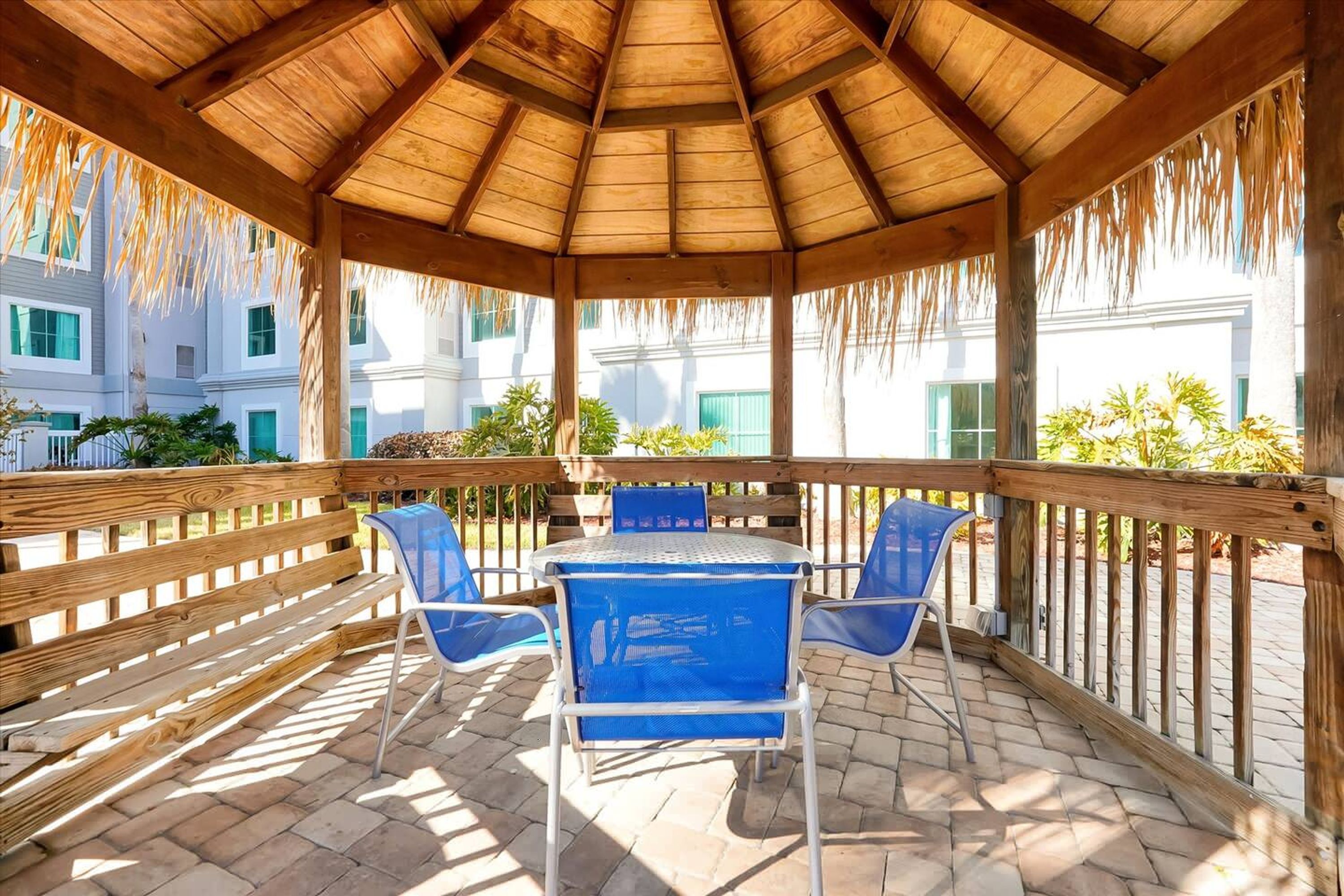 A covered outdoor seating area with a wooden roof, a table, and blue chairs.