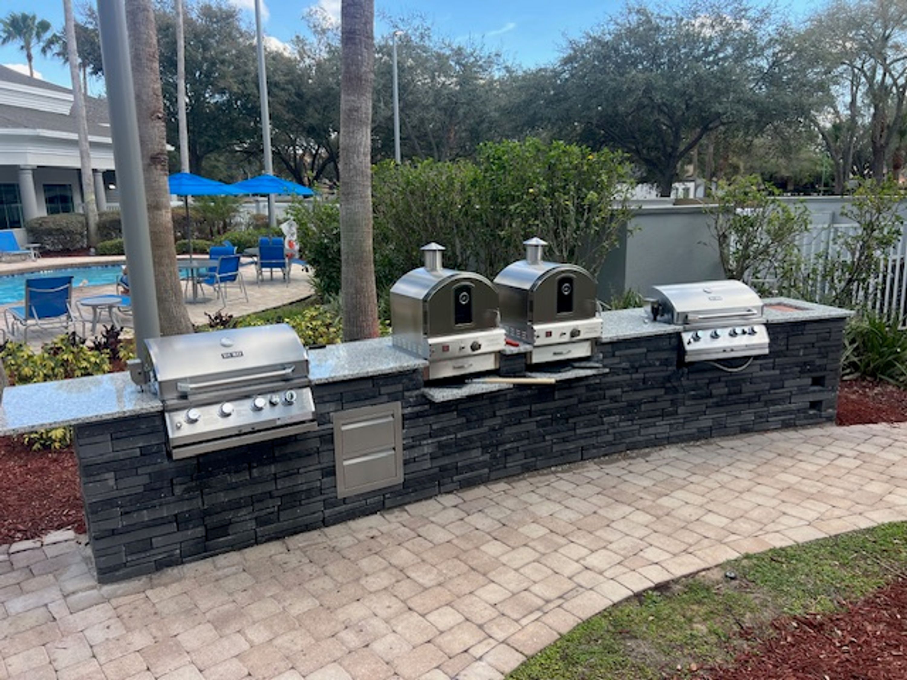 Uma área de churrasco ao ar livre com uma parede de pedra, uma piscina e cadeiras de lounge.