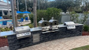Un área de barbacoa al aire libre con pared de piedra, piscina y sillas de descanso.