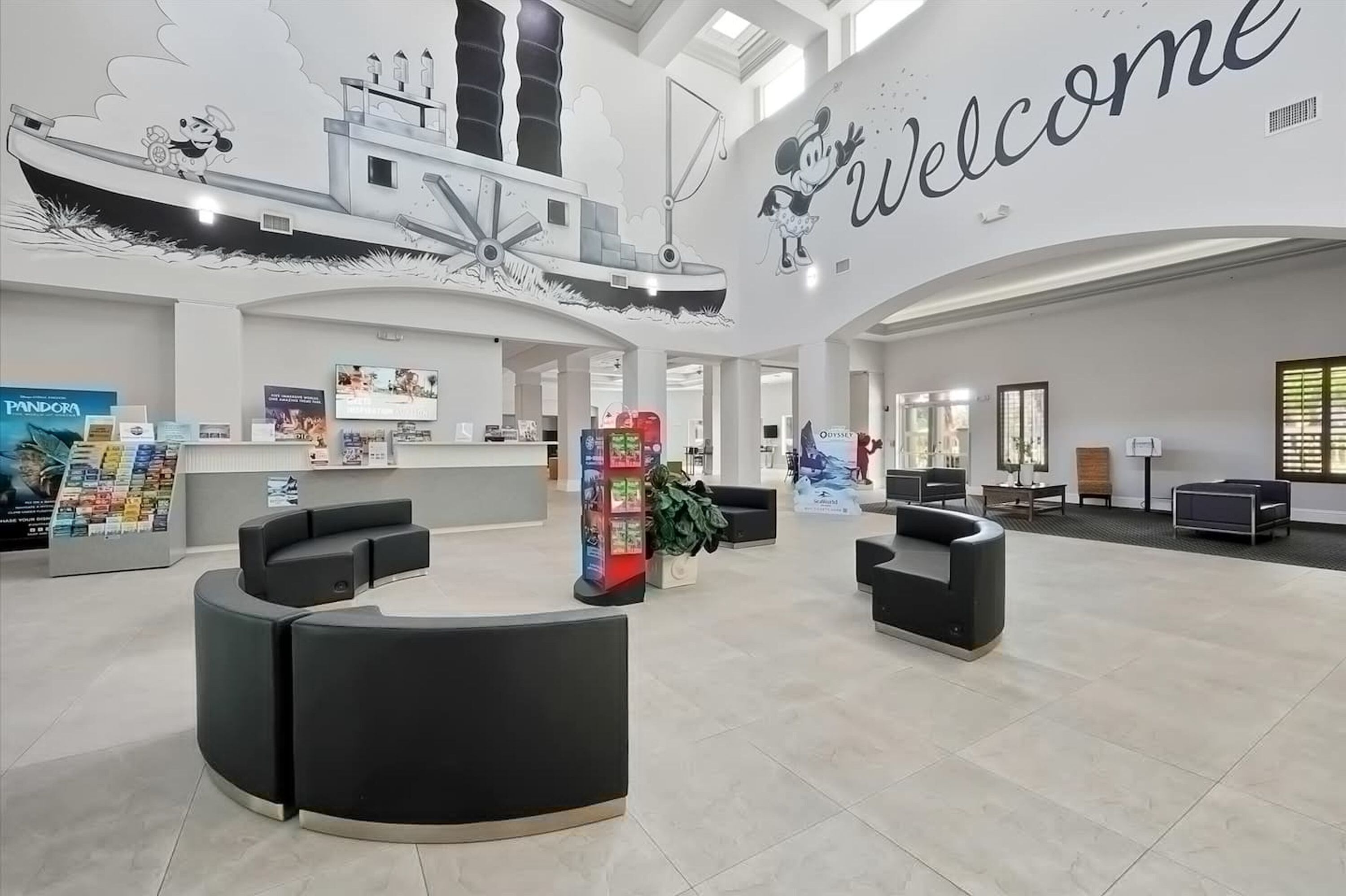 Um lobby espaçoso com um grande letreiro 'Welcome', áreas de estar com assentos pretos e um mural com tema náutico na parede.