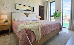 Un dormitorio con una cama, dos mesitas de noche con lámparas, un ventanal y vistas al exterior.