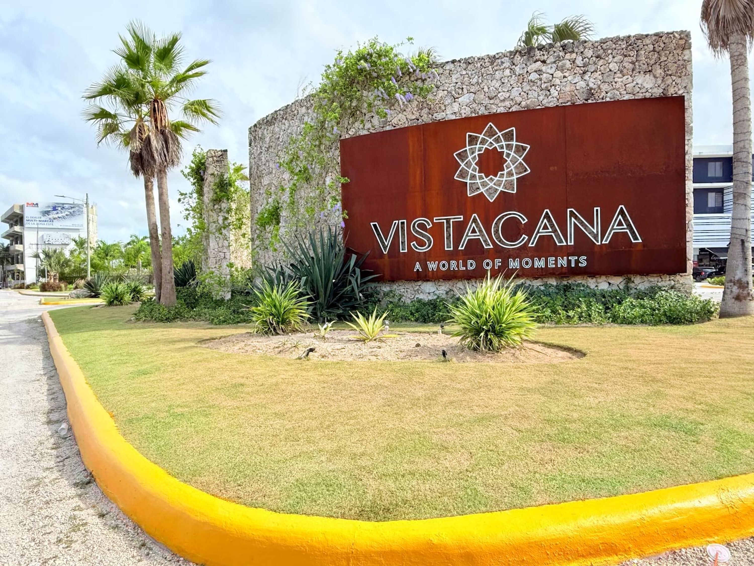 Un senyal per a 'Vistacana' amb un logotip, envoltat d'una zona enjardinada amb gespa i plantes.
