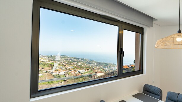 Ein Zimmer mit großem Fenster, einem Esstisch und einer Pendelleuchte.