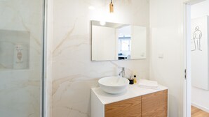 Ein modernes Badezimmer mit einem weißen Waschbecken, einem Holzschranken und einem großen Spiegel.