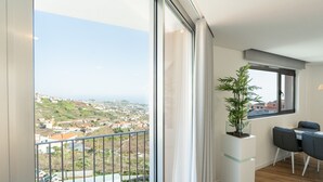 Ein Balkon mit Blick auf eine Stadt und das Meer, ein Essbereich mit Tisch und Stühlen sowie ein Blumentopf.