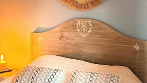 Ein Bett mit Holz-Kopfteil, zwei Kissen mit Muster und einem gewebten Wandbehang.