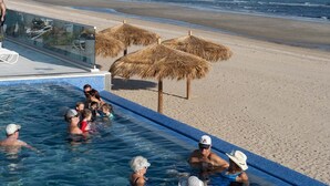 Una piscina con barrera de cristal, sombrillas de playa y vistas al océano.