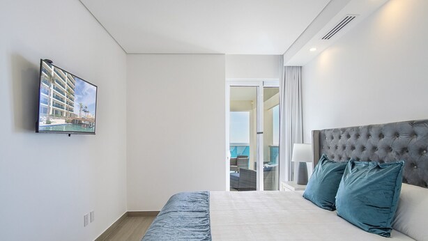 Habitación de hotel con cama, televisor montado en la pared y vista a la piscina y al edificio exterior.