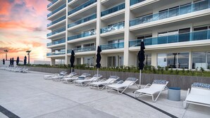 Un hotel moderno con varios balcones, sillas de tomar el sol y sombrillas.