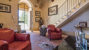 Un intérieur spacieux avec un escalier, des fauteuils en cuir, des têtes d’animaux empaillées accrochées aux murs et un tapis à motifs zébrés.