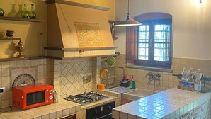 Uma cozinha com painel de azulejos, vigas de madeira, micro-ondas vermelho, fogão a gás e ilha de pedra.