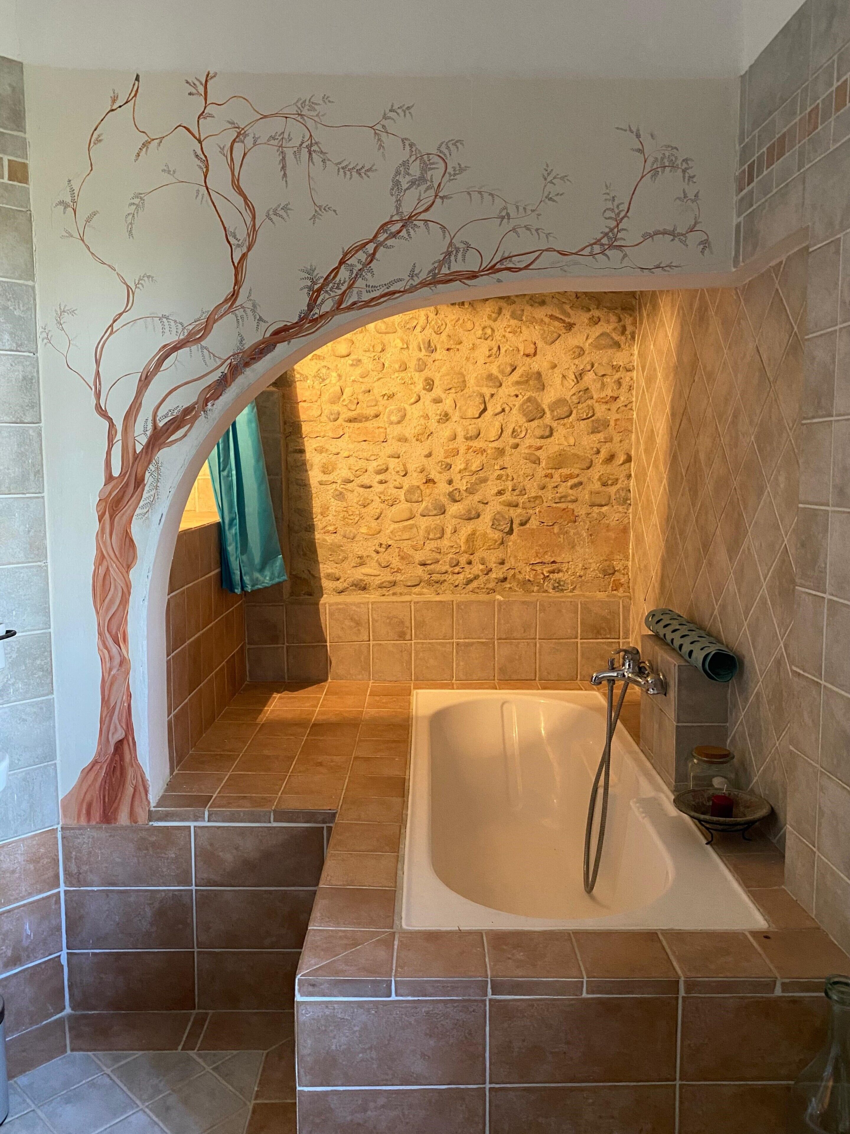Un bany amb paret de pedra, banyera i mural d'un arbre a la paret.