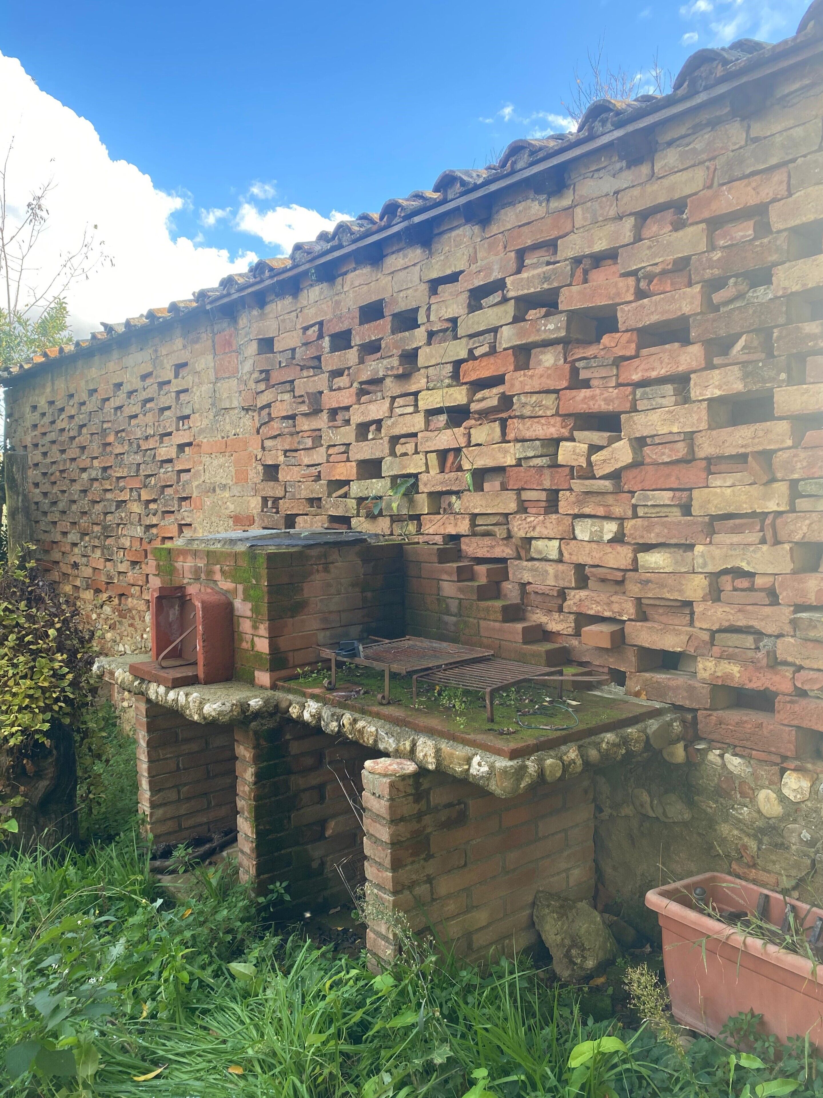Un mur de maó amb una construcció petita i desgastada, envoltat per vegetació exuberant.