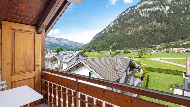 Un balcon doté d’une balustrade en bois, d’une table blanche et offrant une vue sur une montagne et des immeubles d’habitation.