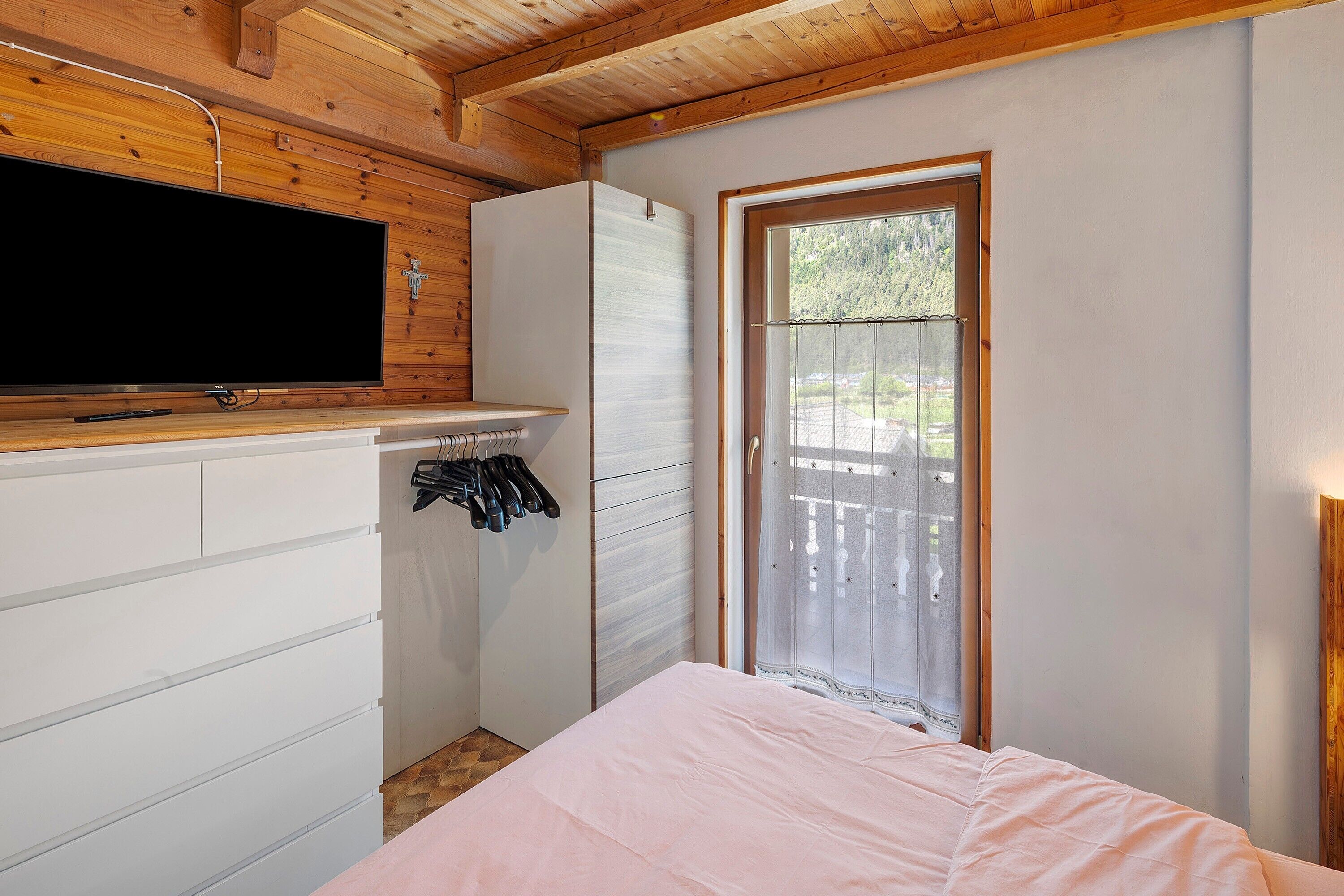 Ein Schlafzimmer mit Bett, Fernseher, Kleiderschrank und Fenster.