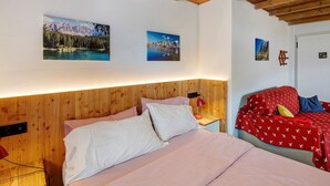 Une chambre à coucher avec une tête de lit en bois, un lit recouvert d’une literie blanche et rouge, et deux tableaux encadrés accrochés au mur.
