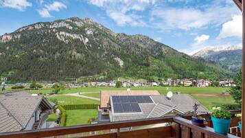 A mountain view from a balcony with solar panels on the roof, a wooden railing, and a potted plant.