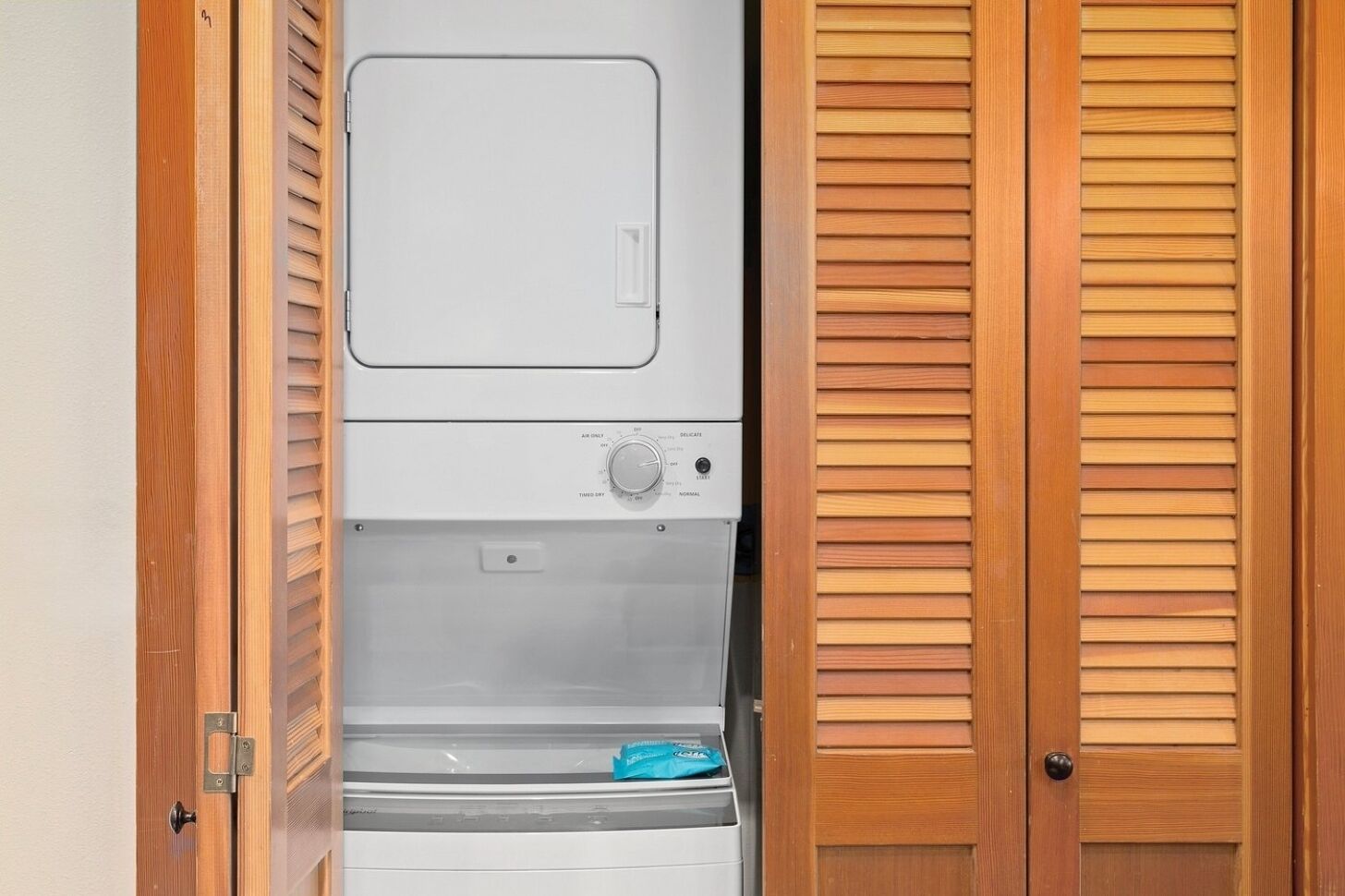 A laundry room with a washing machine, dryer, and wooden louvered closet doors.