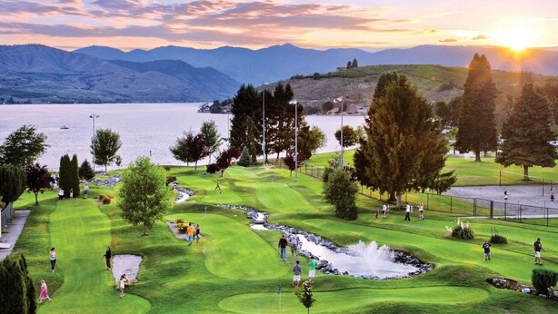 Ein Golfplatz mit einem See und Bergen im Hintergrund.