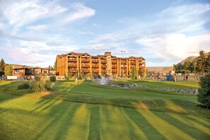 A large, multi-story hotel with a central courtyard, surrounded by lush greenery and a mountainous backdrop.