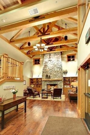 A spacious room with a stone fireplace, wooden beams, and a staircase.
