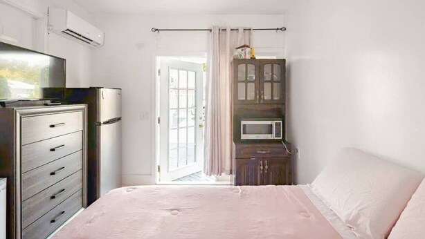 A bedroom with a bed, a dresser, a TV, a microwave, and a door leading to a balcony. - Room-private Studio Apartment in Vero Be (Vero Beach)