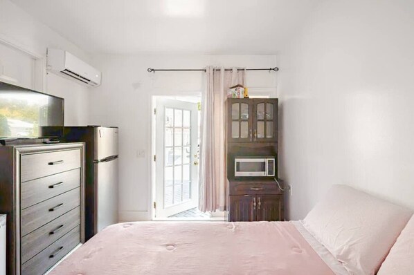Une chambre à coucher comprenant un lit, une commode, un téléviseur, un four à micro-ondes et une porte donnant sur un balcon.