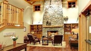 A spacious room with a stone fireplace, wooden beams, and a staircase. - Lake Ozarks | Family Lake Retreat | Pool + Lake | 3BR Sleeps 8 (Chelan)