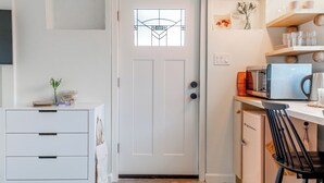 A compact kitchen with a white door, a small refrigerator, a microwave, and a chair. - Designer E Austin Studio Close to Airport, Downtown, & UT Campus (Austin)